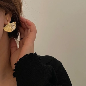 Golden ginkgo leaf stud earrings with metallic texture worn by a model on a beige background