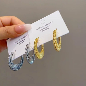 Close-up of gold and silver textured C-hoop earrings with 925 silver needles