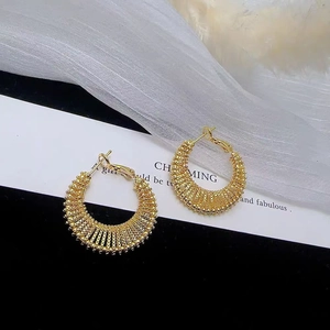 Golden woven mesh hoop earrings on elegant background with white veil and decorative card