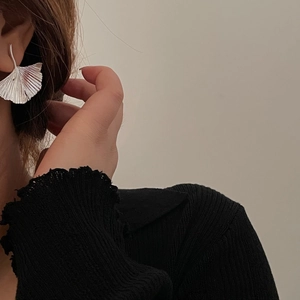 Detailed view of silver ginkgo leaf earrings with radial texture on a model ear