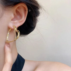 Close-up of a large gold heart hoop earring with textured finish on a model