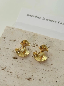 Detail of gold fan-shaped geometric earrings with hammered texture on travertine stone