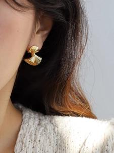 Close-up of golden irregular geometric earrings with hammered texture on a model