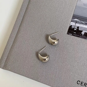 Polierte silberne geometrische Tropfenohrstecker vor minimalistischem Hintergrund