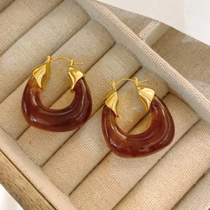 Detail of amber marble resin drop earrings with golden metal edging on beige velvet