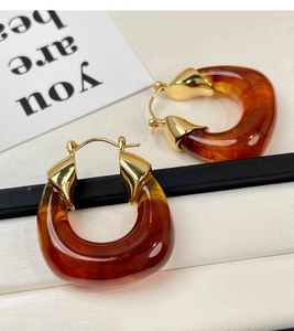 Macro view of amber resin C-shape earrings with gold accents on a textured background