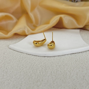Macro detail of gold teardrop stud earrings with a polished mirror finish on silk