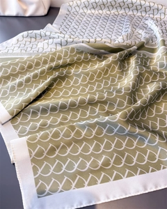 Close-up of olive and beige silk scarf featuring premium monogram pattern and satin texture
