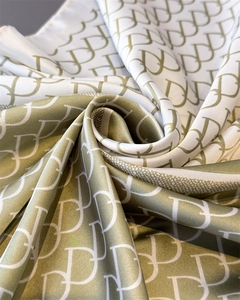 Detail of silk-like satin scarf featuring olive green monogram print and elegant texture