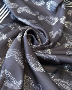 Nahaufnahme eines Seidenschals mit grauem Paisleymuster und eleganter Streifenkante