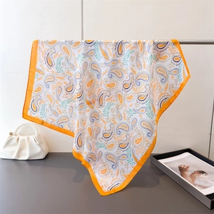 Orange Paisley printed silk scarf hanging gracefully with a pearl bag and magazine