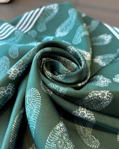 Makroaufnahme eines dunkelgrünen Seidenschals mit Paisley-Muster in Rosenform gerollt