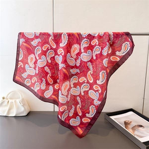 Close-up of red paisley silk scarf with satin border hanging on a metal display stand