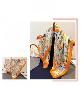 Dettaglio macro di un foulard quadrato in seta con stampa floreale e bordo arancione acceso