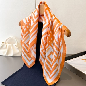 Orange and white geometric silk-like scarf draped over a navy top in an elegant setting