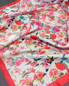 Dettaglio di un foulard di seta a fiori con bordi rossi vivaci e una consistenza liscia