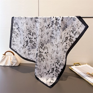 Dettaglio del foulard in seta con stampa floreale e bordo nero appeso alla gruccia