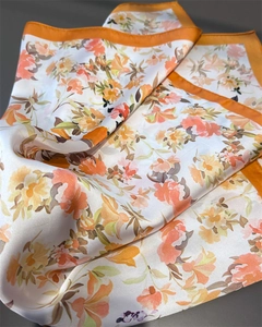 Dettaglio del foulard floreale in seta con bordo arancione e trama in raso lucido