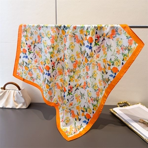 Dettaglio di un foulard in seta floreale con bordo arancione drappeggiato su un'asta