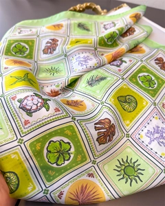 Detailed close-up of green silk square scarf with nature prints on a golden vintage tray