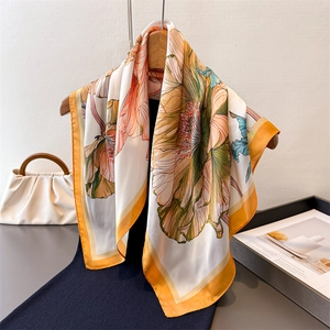 Elegant floral silk-feel square scarf with orange and beige botanical prints on a hanger