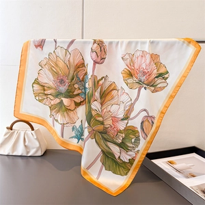 Macro detail of elegant floral print silk square scarf with vibrant orange hand-rolled edge
