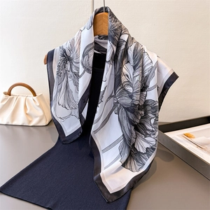 Elegant black and white floral printed silk square scarf draped on a wooden hanger