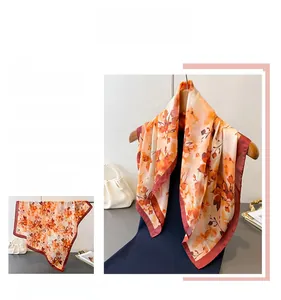 Détail d'un foulard en soie à fleurs orange avec bordure rouge foncé sur un cintre doré