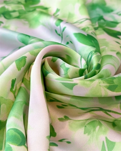 Vue macro d'un foulard en soie à fleurs vertes torsadé en rose montrant sa texture satinée