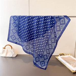 Détail d'un foulard en soie bleu marine à pois blancs et bordure losange géométrique