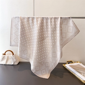 Détail du foulard en soie beige à pois géométriques drapé sur un support en métal