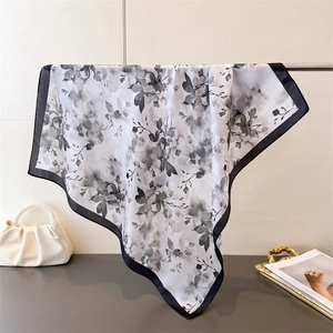 Carré en soie aux motifs floraux et bordure noire présenté sur un sac de luxe chic