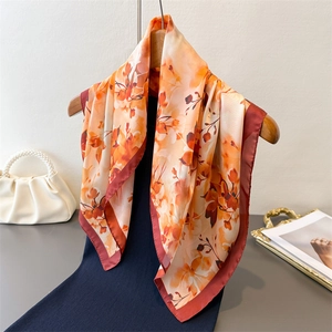 Gros plan d'un foulard carré en soie à imprimés floraux orange sur un cintre