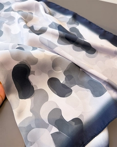 Close-up of silk square scarf featuring grey abstract patterns and navy hemmed edges