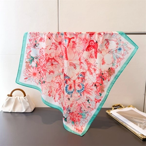 Detailed view of large floral butterfly silk scarf with mint green border on a metal rack