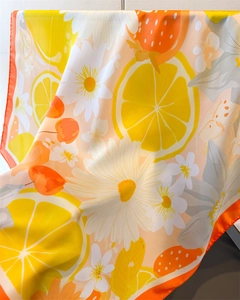 Détail d'un foulard en soie synthétique avec imprimé citron et fleurs et bord orange