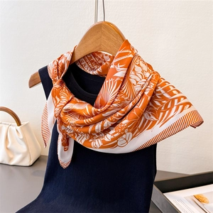 Detail of vibrant orange silk scarf with white tropical leaf prints and striped borders