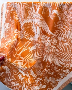 Detail of silk square scarf featuring orange tropical floral print and smooth satin texture