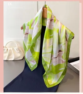 Détail du foulard satiné à motif de feuilles vert citron sur un cintre en bois naturel