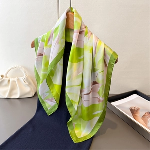 Détail d'un élégant foulard en soie vert à motif floral avec un sac à poignée perle
