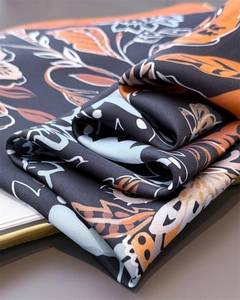 Close-up of floral print silk scarf with black, orange, and blue botanical patterns