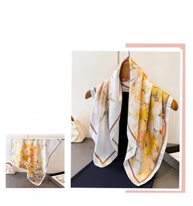 Detailed view of square silk scarf with orange floral prints and smooth satin texture