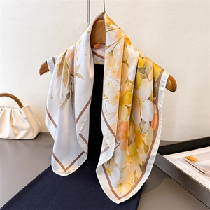 Elegant square silk scarf with yellow floral print on a wooden hanger with a beige handbag