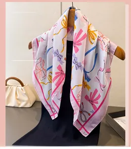 Detail view of the silk-like square scarf featuring bow and pearl prints on a wooden hanger