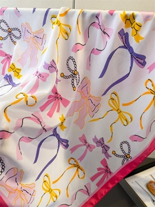 Close-up of silk scarf with colorful bow prints, pearl patterns, and pink borders