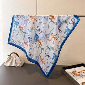 Close-up of silk square scarf featuring colorful bow tie prints and pearl chain details