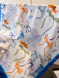 Detail of silk-like scarf featuring colorful bow prints and bright blue satin borders