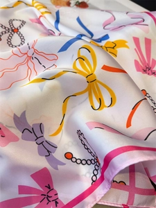 Detailed view of silk-like scarf featuring colorful bows and pearl chain pattern