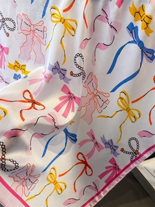 Detailed view of silk square scarf featuring colorful bow prints and pearl patterns