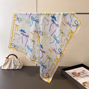 Detail of silk square scarf featuring elegant bow and pearl patterns with smooth texture